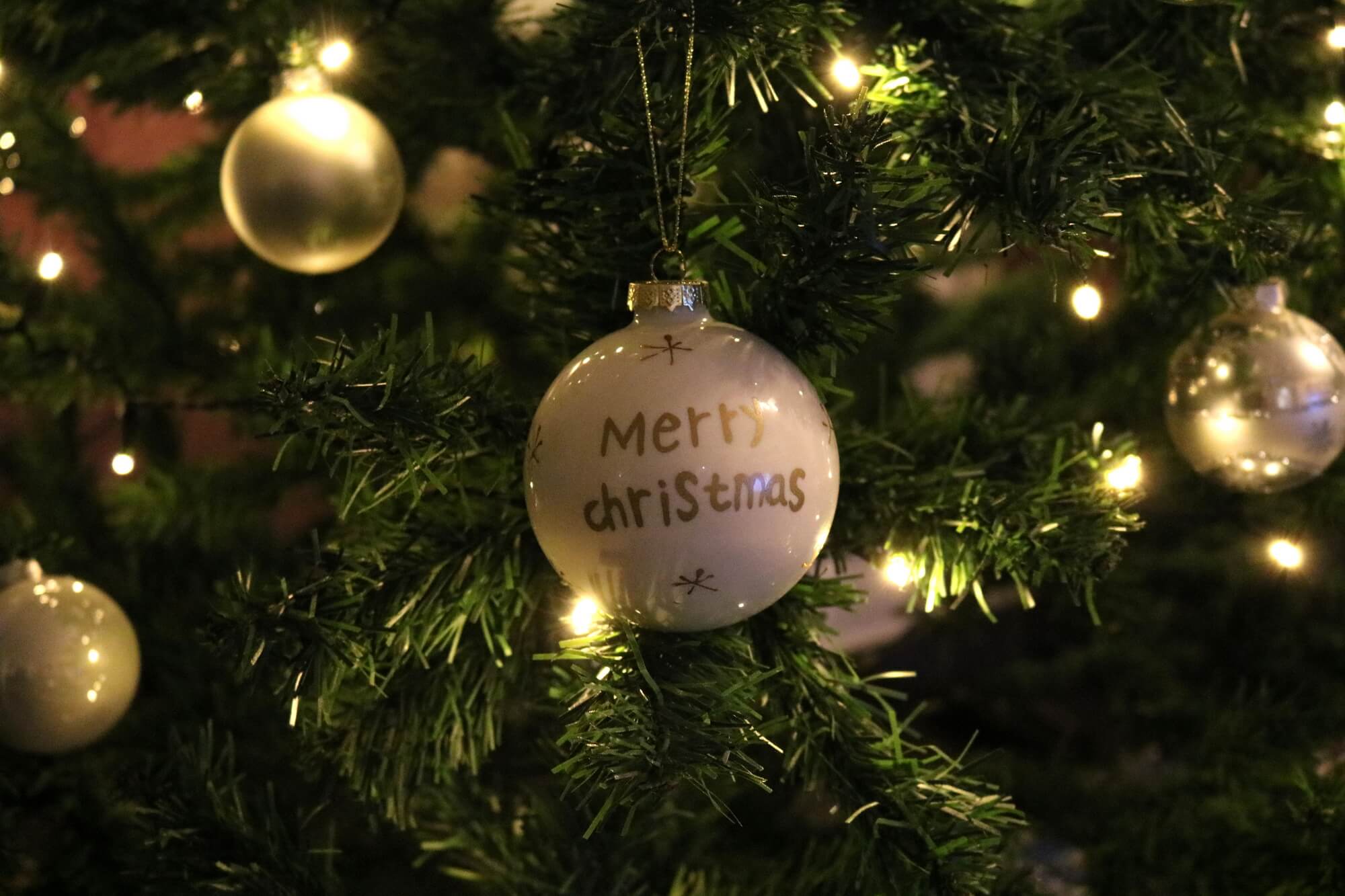 Weihnachtskugel im beleuchteten Weihnachtsbaum mit Schriftzug Merry Christmas