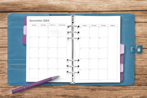 Ein geöffneter Filofax liegt zusammen mit einem Kugelschreiber auf einem Tisch. Die Seiten des Planers zeigen den Kalender mit dem Design "Monat auf 2 Seiten".